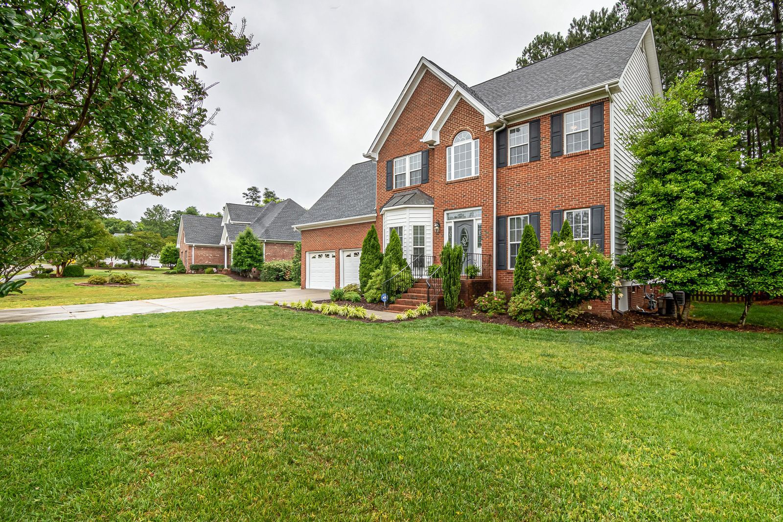Two-story brick home with a manicured lawn and mature shade trees